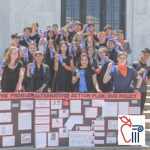 A large group of children display their group project and blue ribbons.