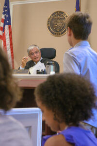 A judge sits at the bench, addressing young students learning about civics and the justice system.